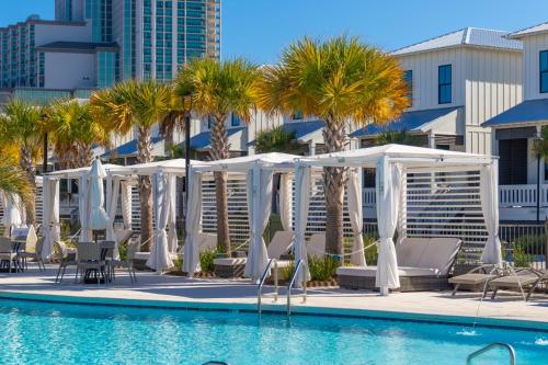 a pool with white umbrellas and chairs and palm trees at Beach Village Resort By Liquid Life in Gulf Shores