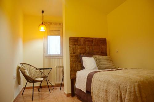 um quarto com uma cama, uma cadeira e uma janela em Ojaranzo em Candeleda