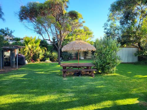 a picnic table with a straw umbrella in a yard at The ReTrO Beach Shack in Aldinga Beach
