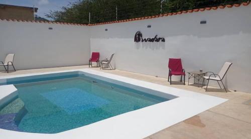 a swimming pool with chairs and a table in front of a white wall at Casa Wadara in La Mira