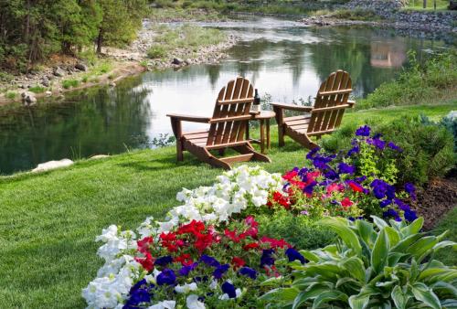 two wooden chairs sitting next to a river with flowers at Haus Hanika in Leavenworth