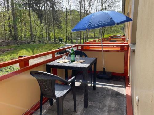 a table and chairs with a blue umbrella on a balcony at Ferienapartment "An der Forellenschänke" in Sebnitz