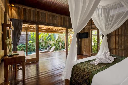 a bedroom with a bed and a desk and windows at The Ulon Ubud Villa in Ubud