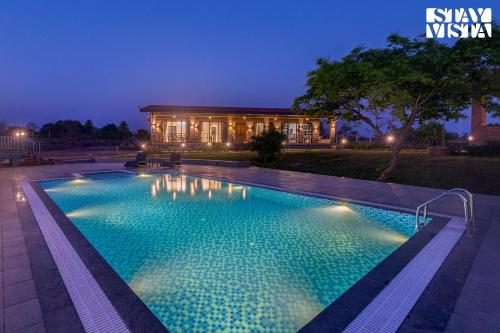 a swimming pool in front of a house at night at StayVistas Nyra Farms - Hill-view villa with Pool, Indoor & Outdoor games, & Lawn with Gazebo in Wada