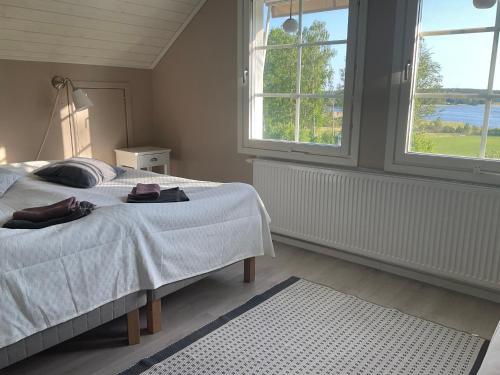 a bedroom with a bed with white sheets and two windows at Villa med sjöutsikt in Fors