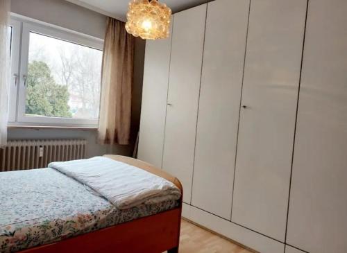 Schlafzimmer mit einem Bett, einem Fenster und einem Kronleuchter in der Unterkunft 1Room in a beautiful shared apartment 12min walk from Center in Friedrichshafen