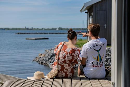 a man and woman sitting on a dock looking at the water at Brouwersdam Stay in Ouddorp