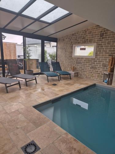 einen Pool auf einer Terrasse mit Stühlen und Ziegelwand in der Unterkunft Villa avec piscine intérieure proche des plages du debarquement in Escoville