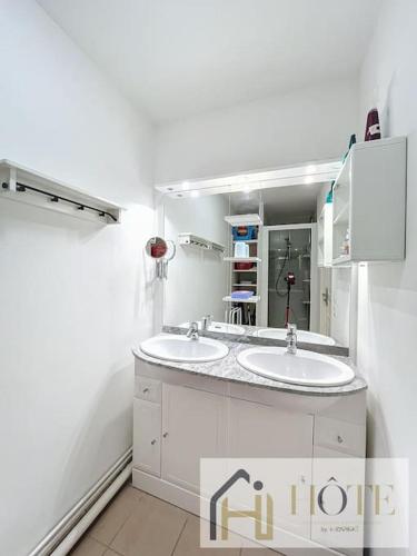 une salle de bain blanche avec deux lavabos et un miroir dans l'établissement Échappée Belle, Confort, Plage et Parking, à Bray-Dunes