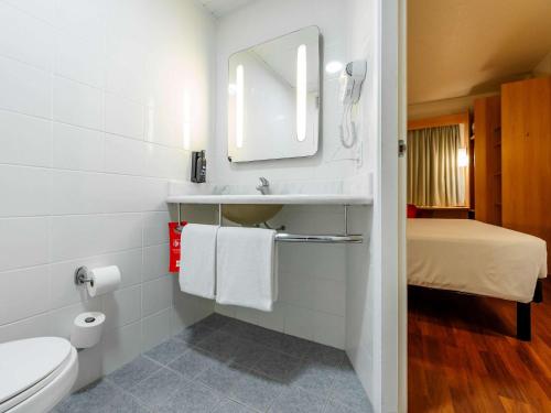 a bathroom with a sink and a toilet and a bed at ibis Joinville in Joinville