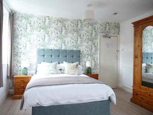 1 dormitorio con cabecero azul y papel pintado con motivos florales en The Cliffbury en Llandudno