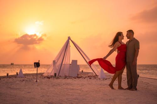 um casal parado na praia ao pôr do sol em Coco Bodu Hithi em Atol de Malé Norte