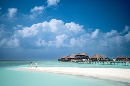 zwei Personen stehen am Strand mit einem Pier in der Unterkunft Coco Bodu Hithi in Nord-Malé-Atoll