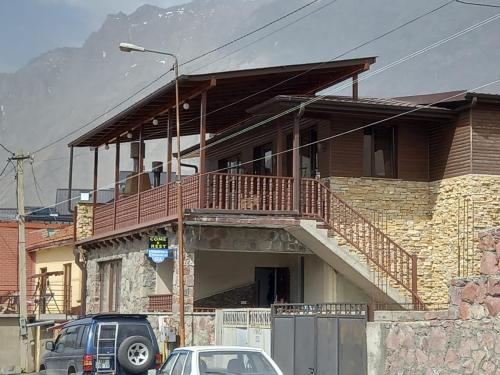 een huis met een balkon en auto's geparkeerd voor het huis bij Come & Rest in Kazbegi