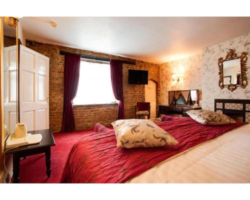 a bedroom with a large bed with red sheets and a window at The Rose And Crown Hotel in Wisbech