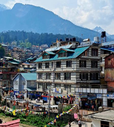 a large building in a city with a mountain at Hotel Snow Mountain Mall Road in Manāli