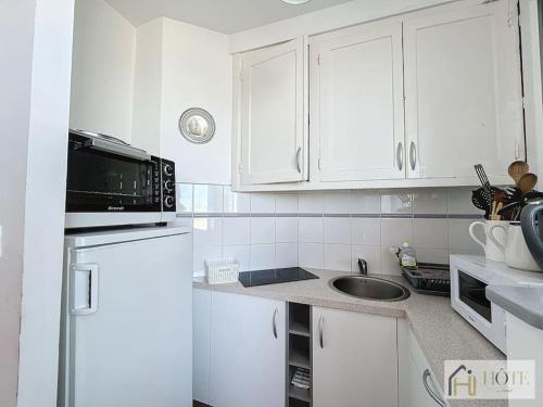 une cuisine blanche avec un évier et un micro-ondes dans l'établissement Nid Mamy: Confort, Mer, Rez-de-Chaussée, à Bray-Dunes