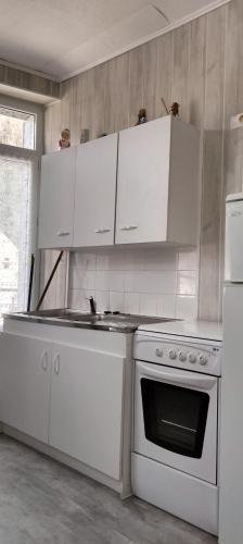 La cuisine est équipée de placards blancs, d'une cuisinière et d'un évier. dans l'établissement Résidence les Sources Mont Dore, à Mont-Dore