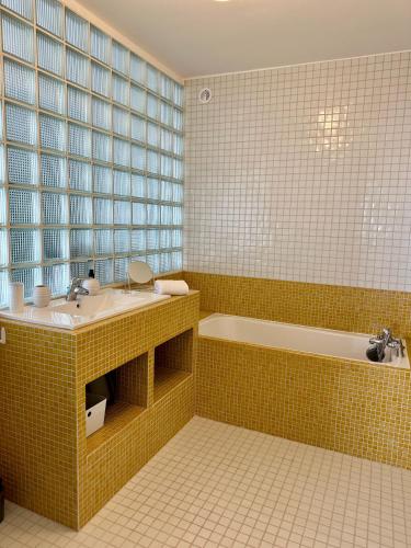 La salle de bains est pourvue de carrelage jaune, d'un lavabo et d'une baignoire. dans l'établissement La Mer à Pied appartement vue mer, à Dieppe