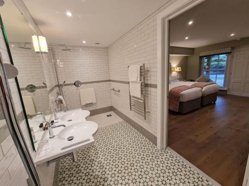 a bathroom with a sink and a bedroom with a bed at Powdermills Country House Hotel in Battle