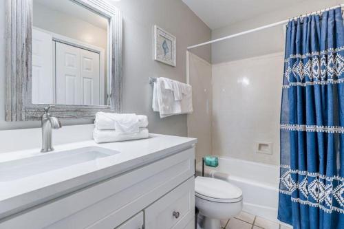 uma casa de banho com um lavatório, um WC e uma cortina de chuveiro azul. em Bonhomme Richard West em Gulf Shores