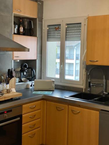 une cuisine avec des armoires en bois, un évier et une fenêtre dans l'établissement Kazeths Chambre chez l'habitant, à Toulouse