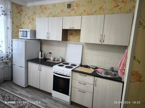 cocina con armarios blancos, fogones y fregadero en Уютная квартира комфорт класса74, en Astana