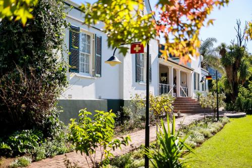 a white house with blue shutters and a yard at Altes Landhaus Country Lodge in Oudtshoorn