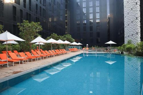 une grande piscine avec des chaises oranges et des parasols dans l'établissement Grand Mercure Dubai City, à Dubaï