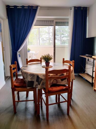 une table à manger avec des chaises et un rideau bleu dans l'établissement Spacieux appartement refait à NEUF - 4 pers - vue sur l'hippodrome, à Cabourg