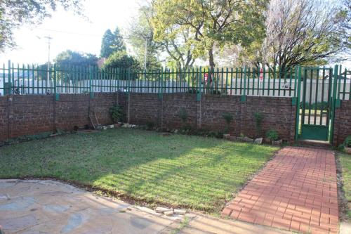 a brick fence with a green gate and a yard at Macum Guesthouse in Roodepoort