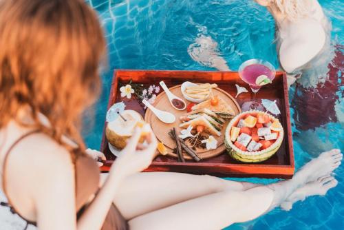 a woman sitting in a pool with a tray of food at Qualia De Hôtel Hoi An - Rooftop Bar City View in Hoi An