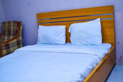 ein Bett mit weißen Kissen und einem Kopfteil aus Holz in der Unterkunft Miccom Golf Hotel and Resort in Ikirun