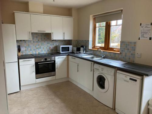 a kitchen with white cabinets and a sink and a dishwasher at Sunbury Aviemore in Aviemore