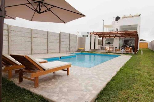 a pool with two chairs and an umbrella next to a house at SOLARIUM CHINCHA Casa de Campo y Playa de 1000mts! in Sunampe