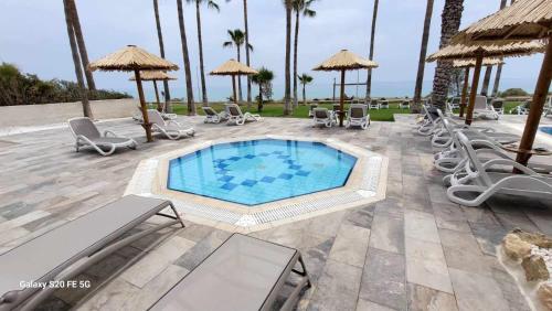 uma piscina com cadeiras e guarda-sóis num pátio em Simos Magic Beach Hotel Apts em Agia Napa
