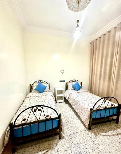 two beds in a bedroom with white walls and blue pillows at Jolie Appt à skhirat 5min de la plage par voiture in Skhirat