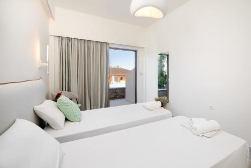 2 letti bianchi in una camera bianca con finestra di Little Corfu a Dassia