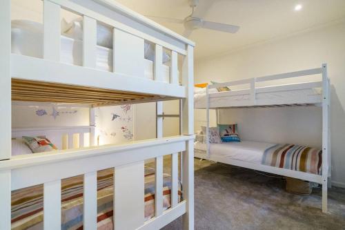 two white bunk beds in a room with a bed at Karinya - Luxurious soul sanctuary by the surf. in Rye