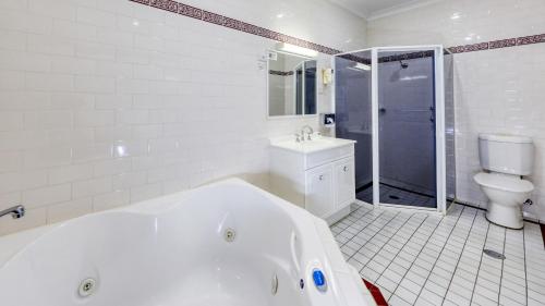 a white bathroom with a tub and a toilet at Breakout Motor Inn in Cowra