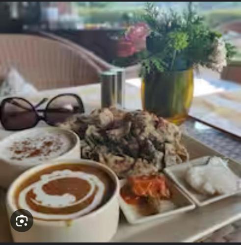 リシケーシュにあるALOHA DIVINE GANGES APARTMENTS with INFINITY POOLの食べ物の皿とコーヒーカップが置かれたテーブル