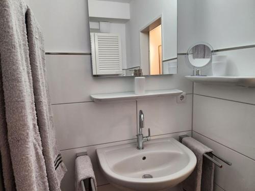 ein weißes Badezimmer mit einem Waschbecken und einem Spiegel in der Unterkunft Sound of the sea Modern retreat in Wangerooge