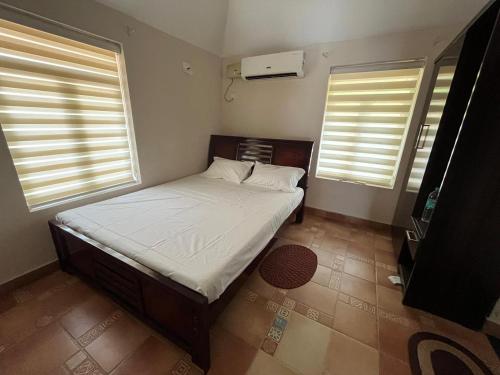 a small bedroom with a bed and two windows at Cocoon Earth Home - Pool Villa Kovalam in Kovalam