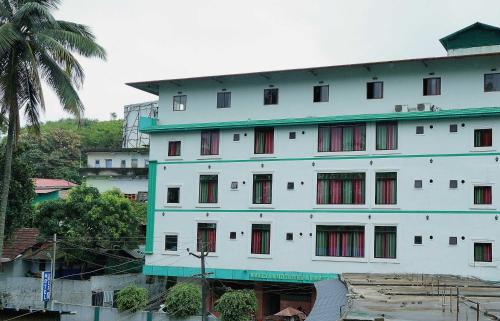 a large white building with red windows and a palm tree at Hotel O Greenland in Meppādi