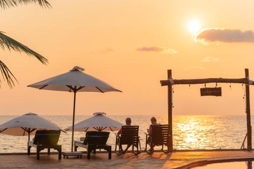 two people sitting in chairs under umbrellas on a beach at Anja Beach Resort & Spa in Phu Quoc