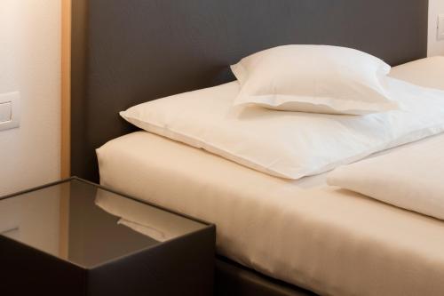 a bed with two white pillows and a glass table at Hotel Schlosswirt in Schenna