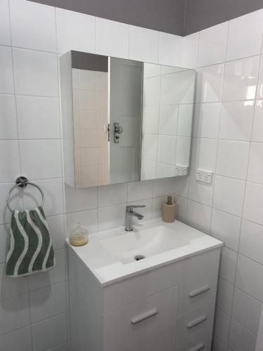 W białej łazience znajduje się umywalka i lustro. w obiekcie Family friendly Katoomba Cottage w mieście Katoomba