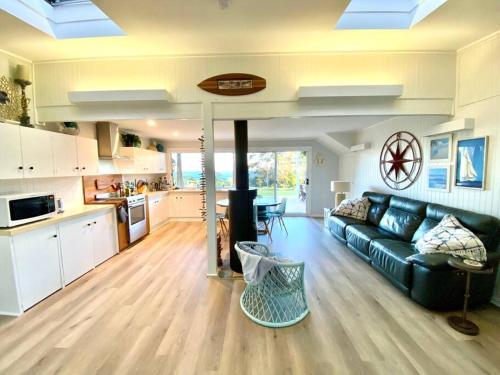 a living room with a black couch and a kitchen at SeaRoos by the Seashore Beach Cottage in Durras