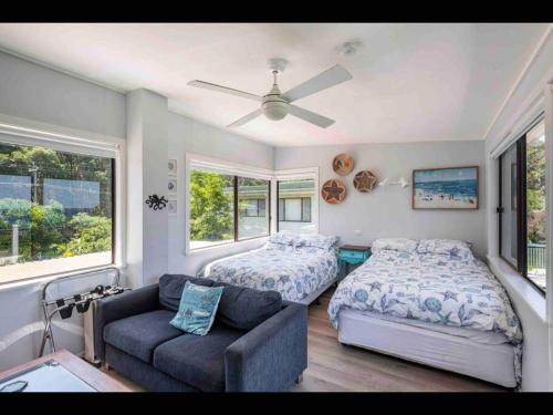 ein Schlafzimmer mit einem Bett und einer Couch und Fenstern in der Unterkunft SeaRoos by the Seashore Beach Cottage in Durras