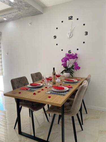 a dining room table with chairs and a clock on the wall at Apartman Pranić Mostar in Mostar